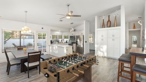 Een moderne keuken met een tafelvoetbaltafel, witte kasten en een eethoek met een tafel en stoelen.