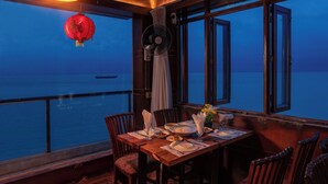 A dining area with a table set for four, overlooking a body of water. - Padma Luxury Resort MawaGhat Dhaka (Louhajang)