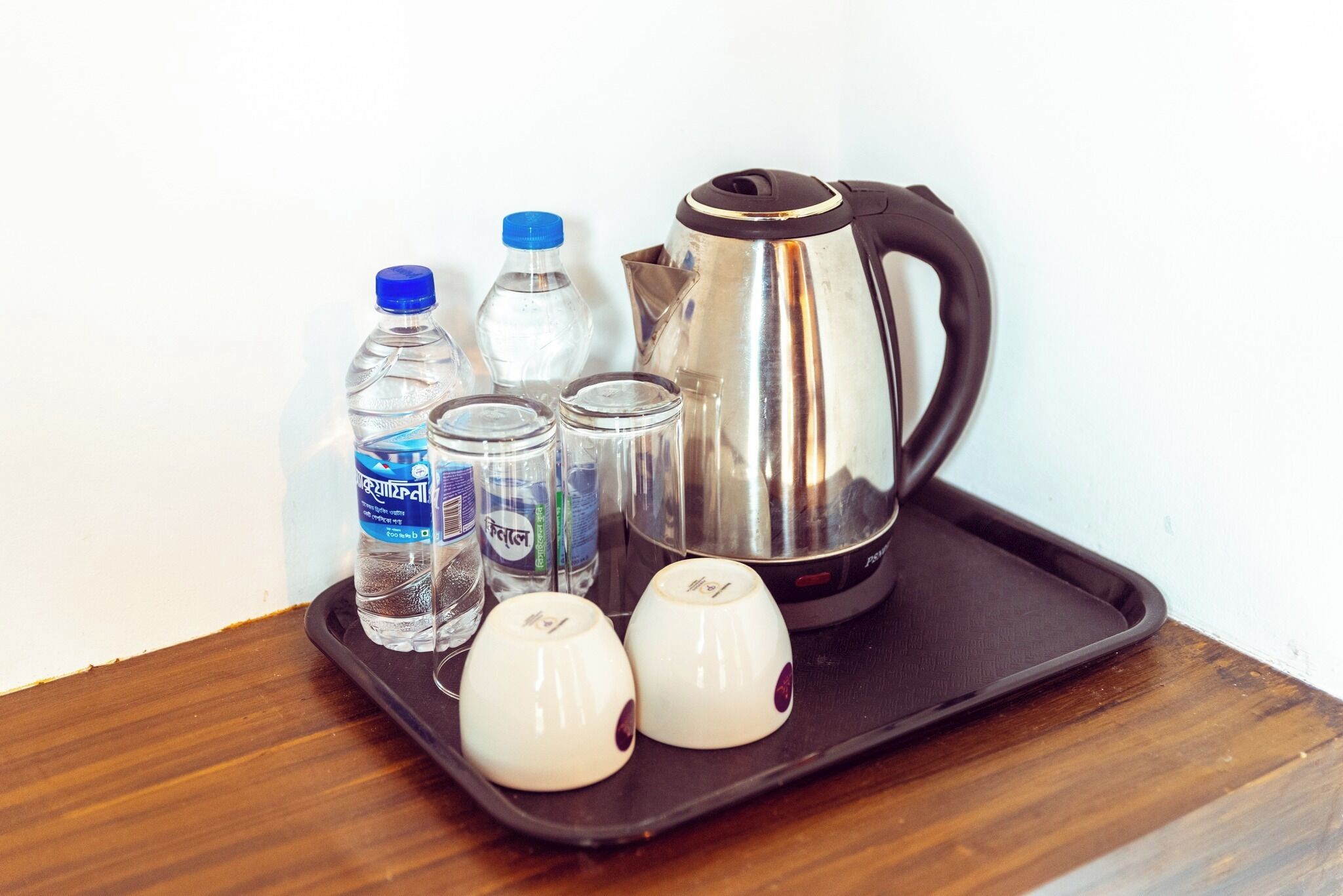 Een dienblad met een waterkoker, twee bekers, twee flessen en twee glazen.