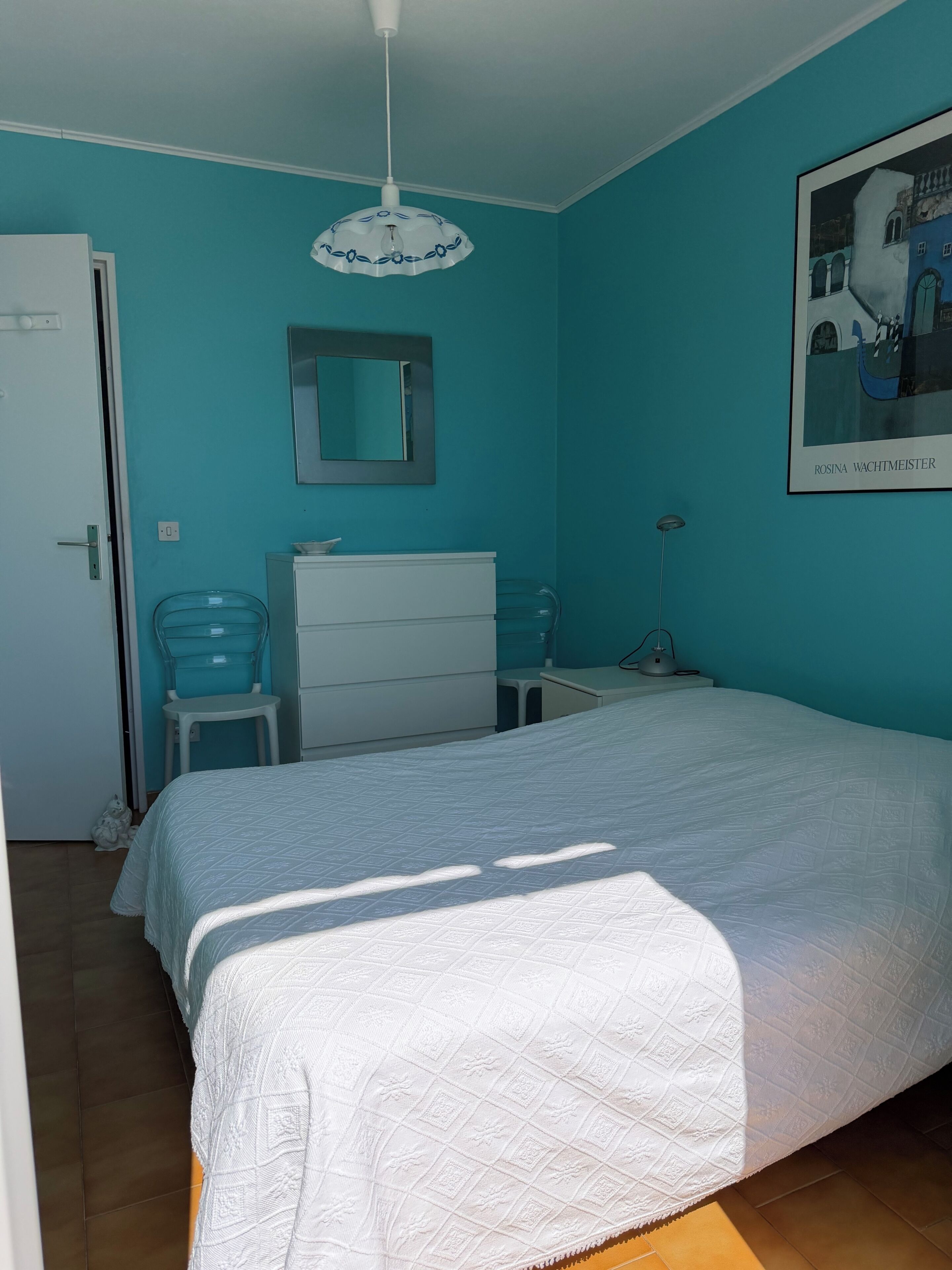 A bedroom with a bed, a dresser, a chair, a desk, a lamp, and a framed picture on the wall.