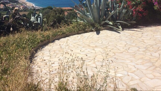 A paved patio with a view of a coastal landscape, including a beach and distant mountains.