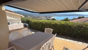 An outdoor patio with a table and chairs, a grill, and a view of a lake and mountains.