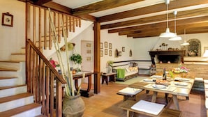 Amplia sala de estar con escalera de madera, chimenea y una mesa de comedor preparada para una comida.