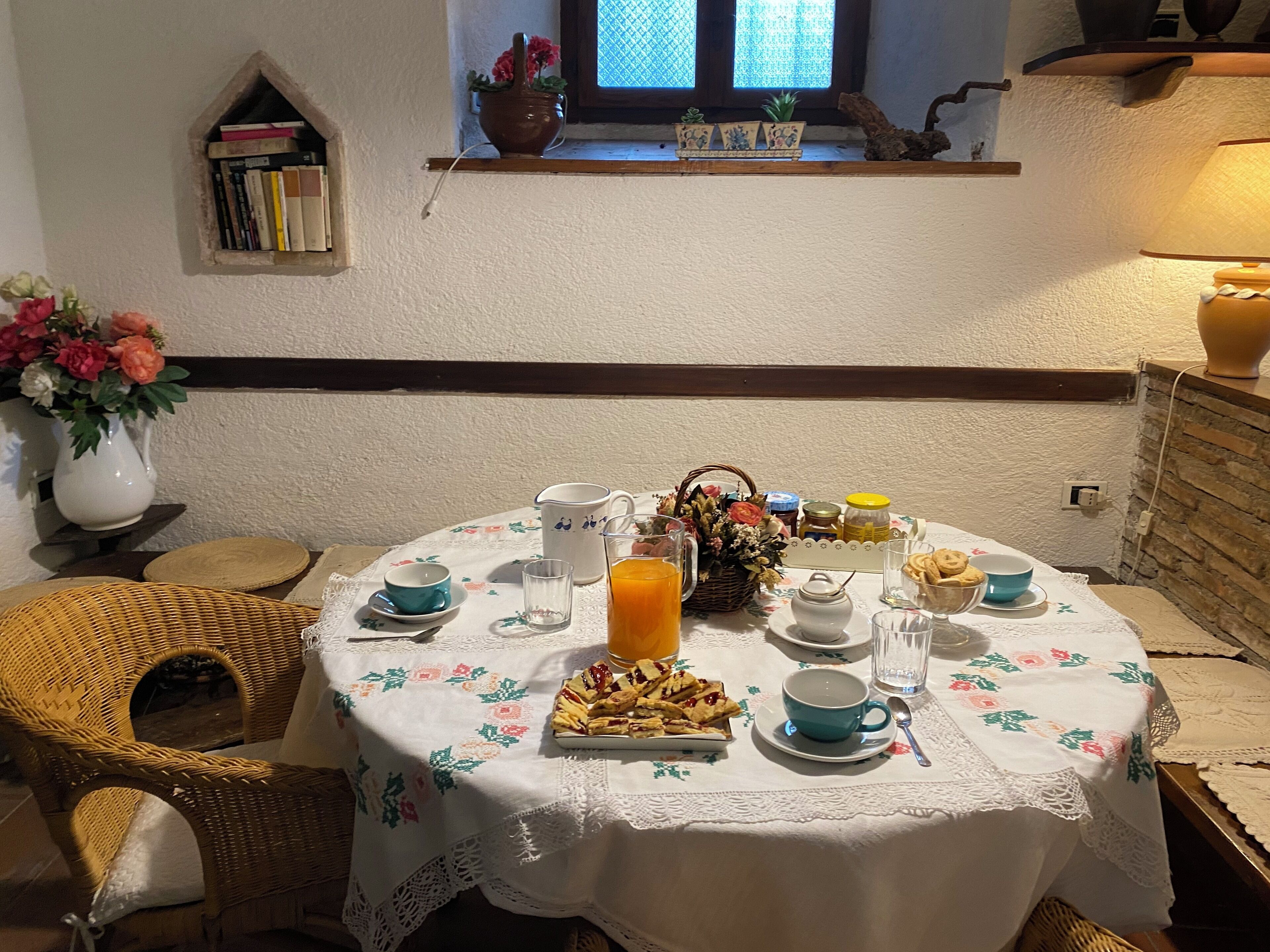 A round dining table with a white lace tablecloth, surrounded by wicker chairs.