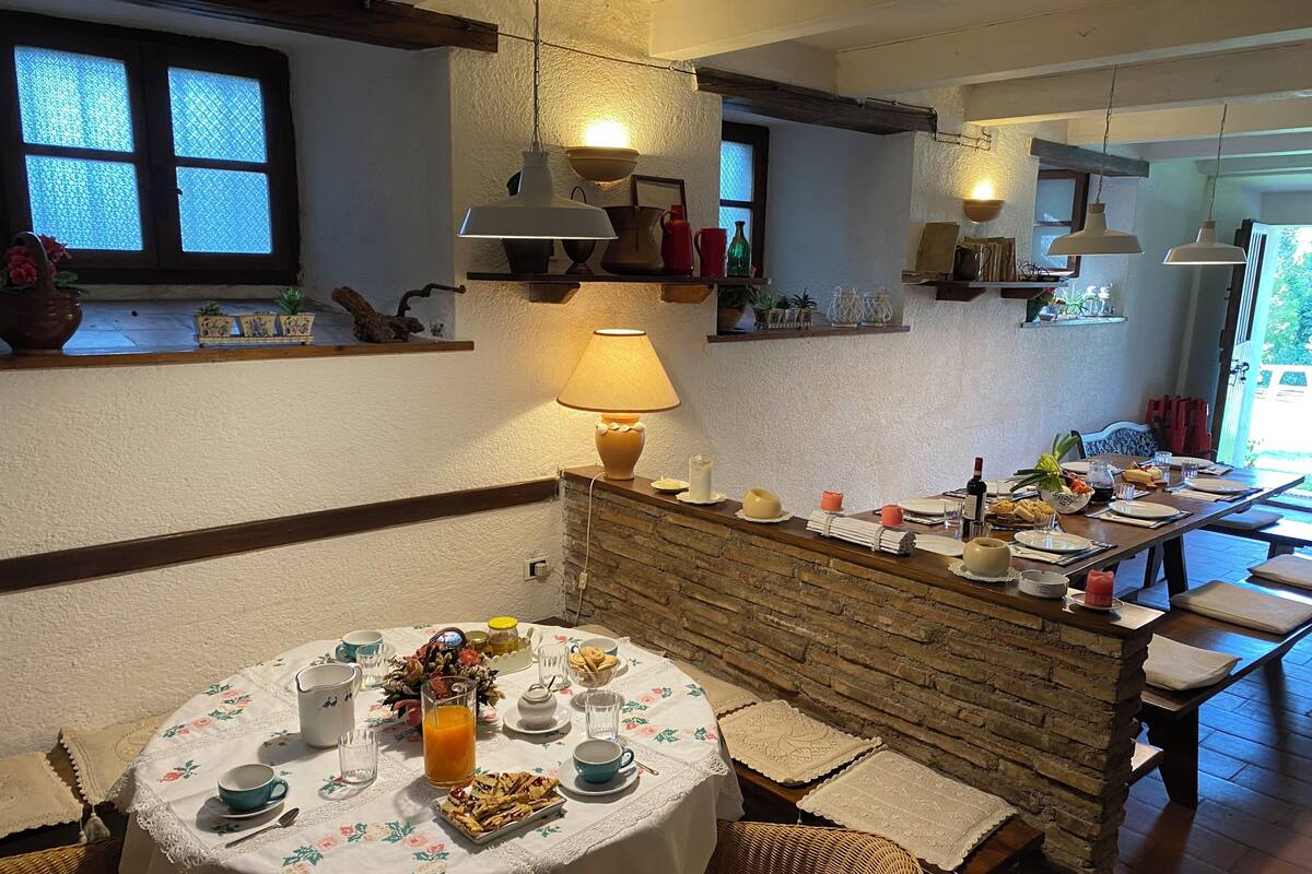 A cozy dining area with a round table set for two, featuring a floral tablecloth, a variety of dishes, and a bottle of wine.