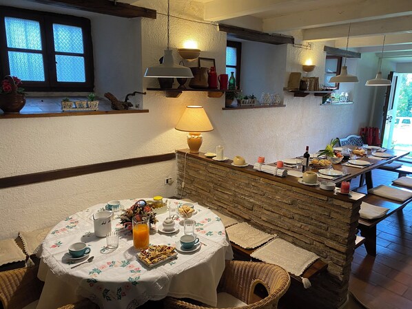 A cozy dining area with a round table set for two, featuring a floral tablecloth, a variety of dishes, and a bottle of wine. - Casa di nonna Nuccia (Fabriano)