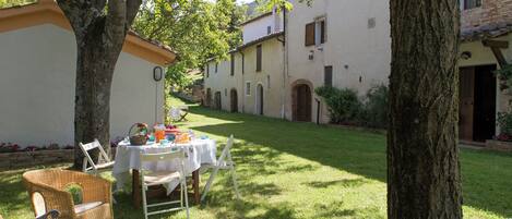 Un patio con una mesa preparada para una comida, rodeado de sillas y una silla de mimbre, con un edificio al fondo.