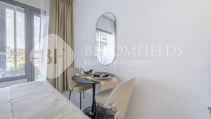 Ein Hotelzimmer mit Bett, Esstisch mit Stühlen, einem Spiegel und Blick durch ein Fenster nach draußen.