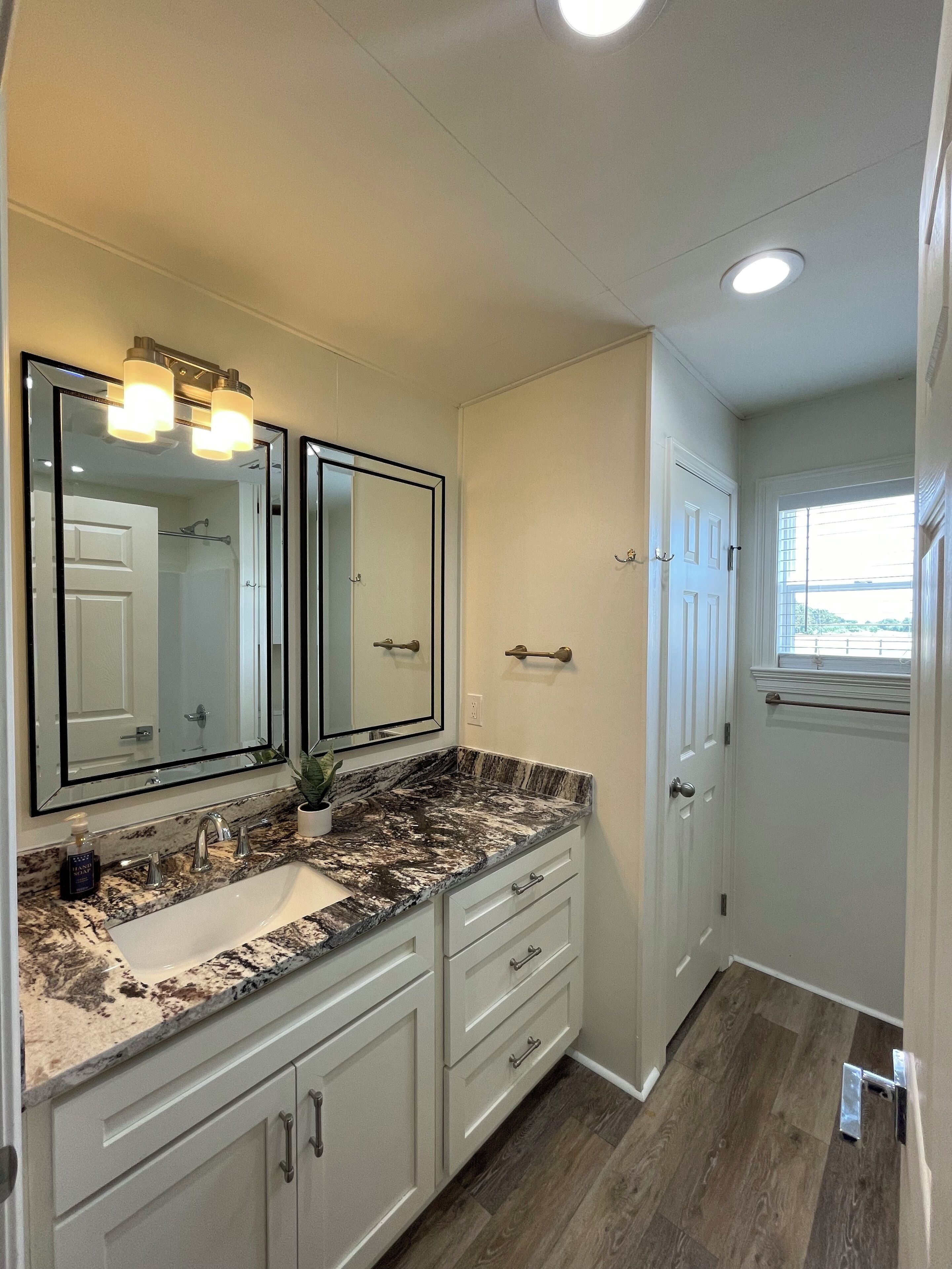 A bathroom with a white vanity, double mirrors, a marble countertop, and a white door.