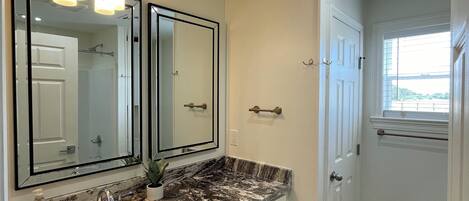 A bathroom with a white vanity, double mirrors, a marble countertop, and a white door.