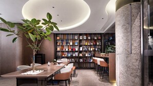 A modern interior with a long wooden table, multiple chairs, a bookshelf, and a large plant. - From.K Hotel (Guangzhou Tianhe Zhengjia Plaza Tiyuxi Road Metro Station Branch) (Guangzhou)