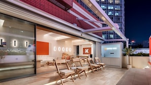 A modern coffee shop with a minimalist interior, outdoor seating, and a view of a high-rise building in the background. - From.K Hotel (Guangzhou Tianhe Zhengjia Plaza Tiyuxi Road Metro Station Branch) (Guangzhou)