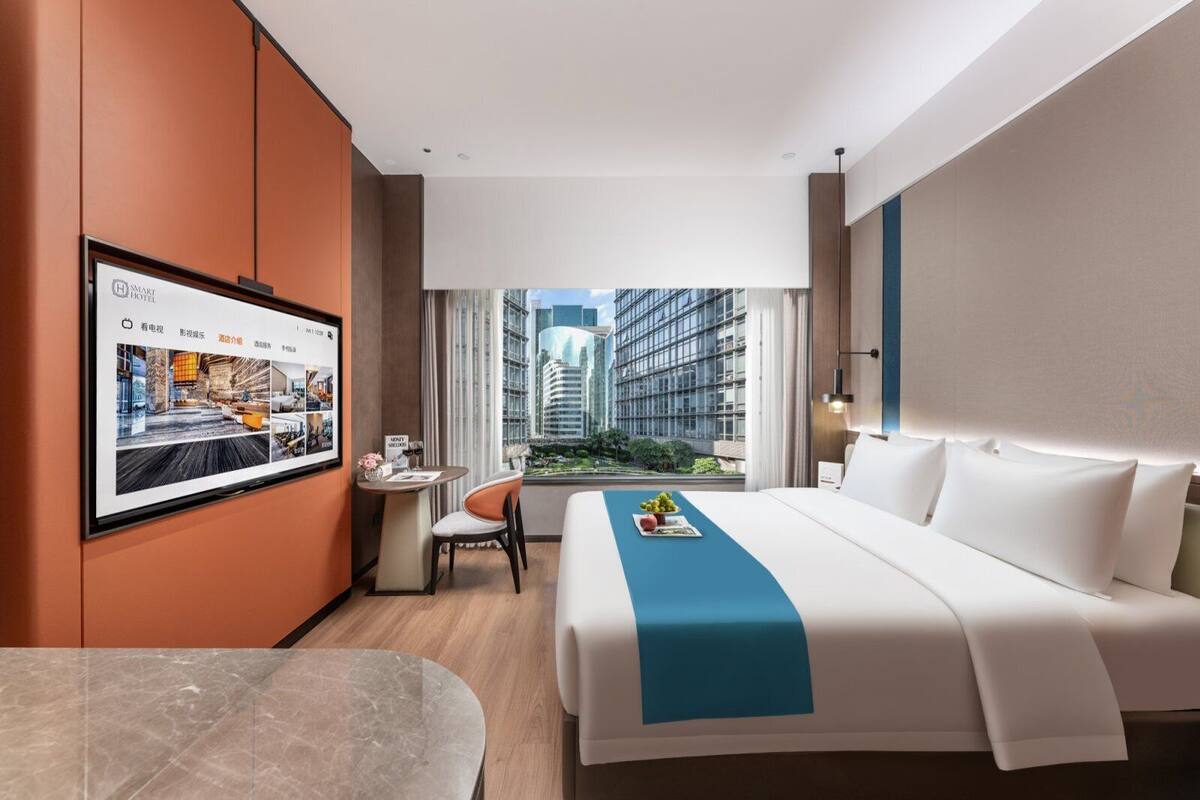 A modern hotel room with a large bed, a desk, and a TV mounted on the wall.