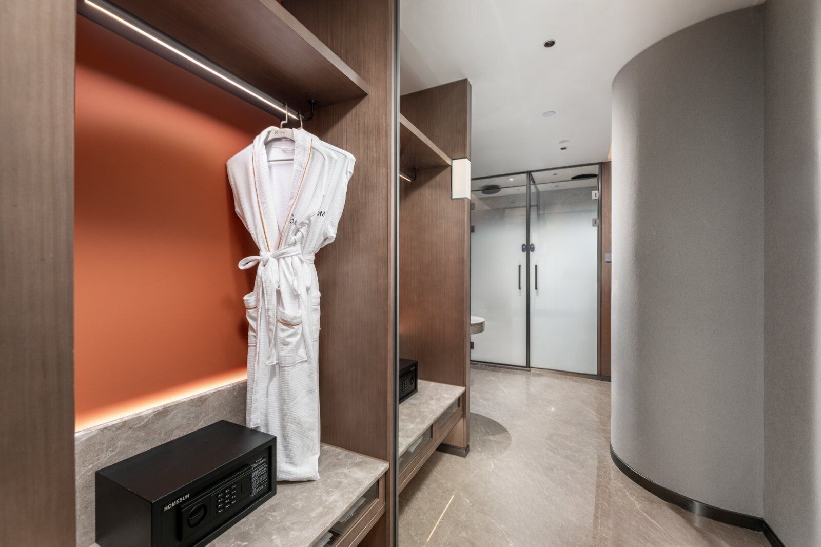 Une salle de bain moderne avec un peignoir accroché au mur, un four à micro-ondes et une cabine de douche en verre.