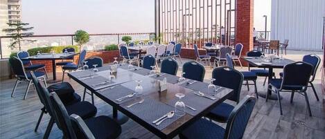 An outdoor dining area with tables and chairs, a brick wall, and a view of the cityscape.