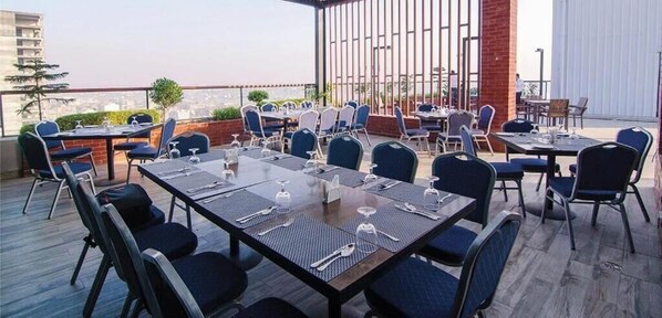An outdoor dining area with tables and chairs, a brick wall, and a view of the cityscape.