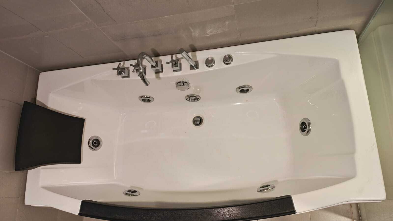 A white bathtub with multiple faucets and a black seat.