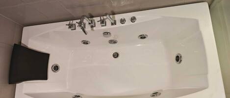 A white bathtub with multiple faucets and a black seat.