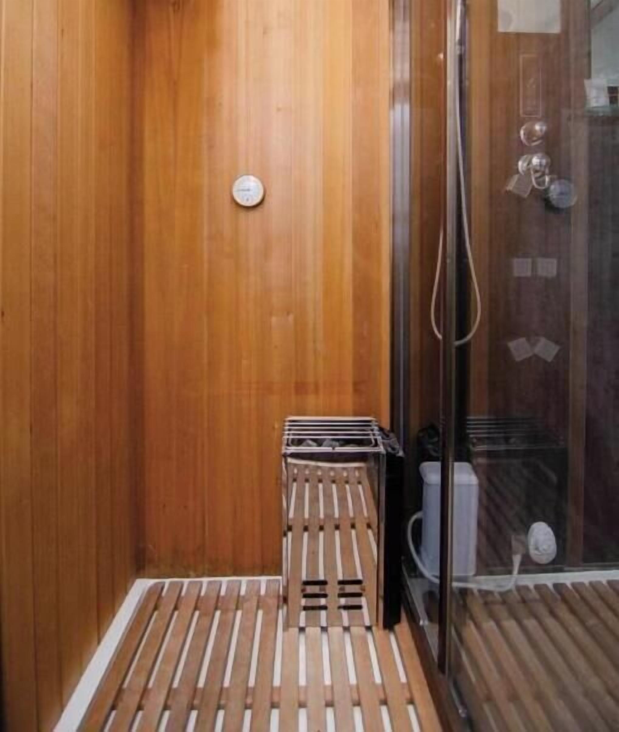 A wooden-paneled bathroom with a shower area, a small wooden stool, and a glass shower door.
