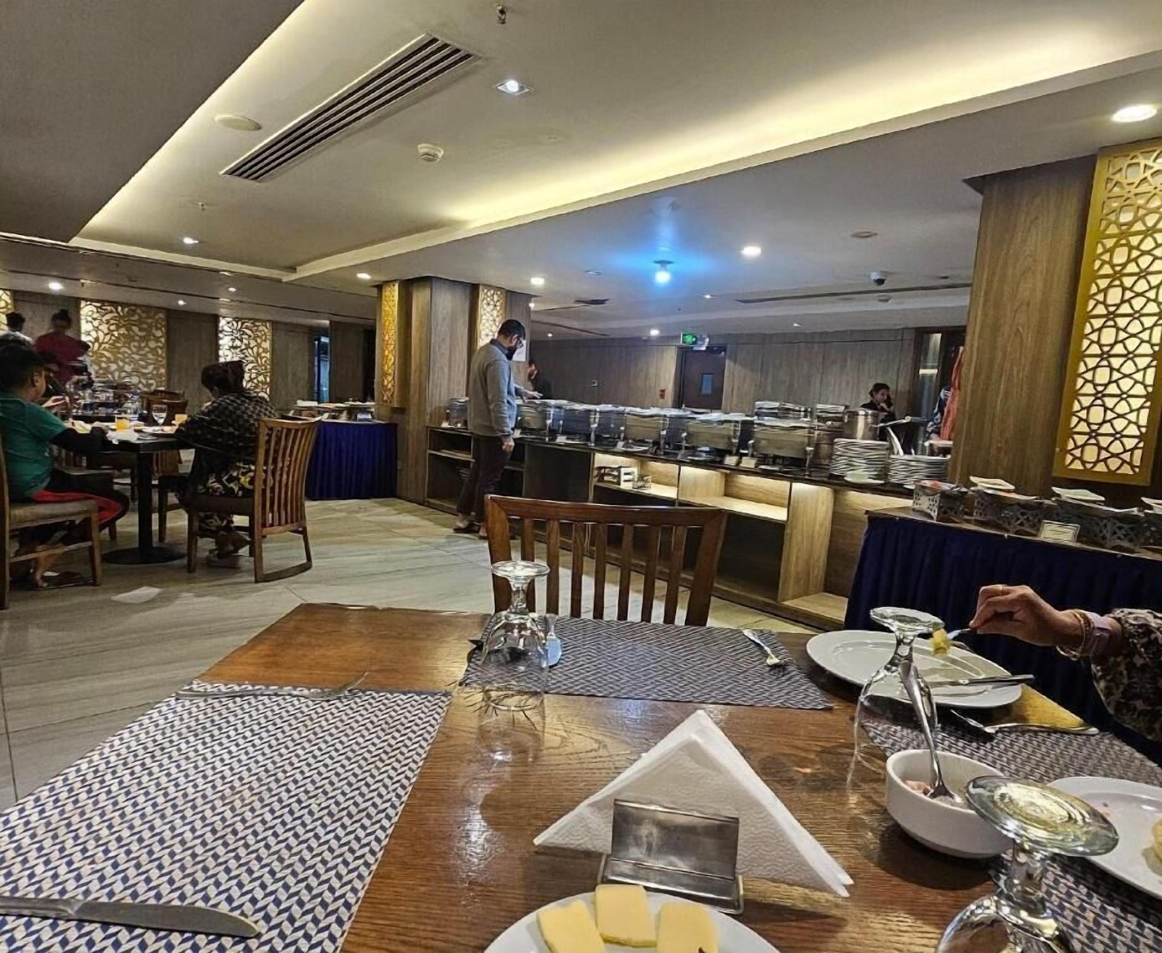 A buffet-style restaurant with multiple dining tables, a central serving area, and a decorative wall with intricate patterns.
