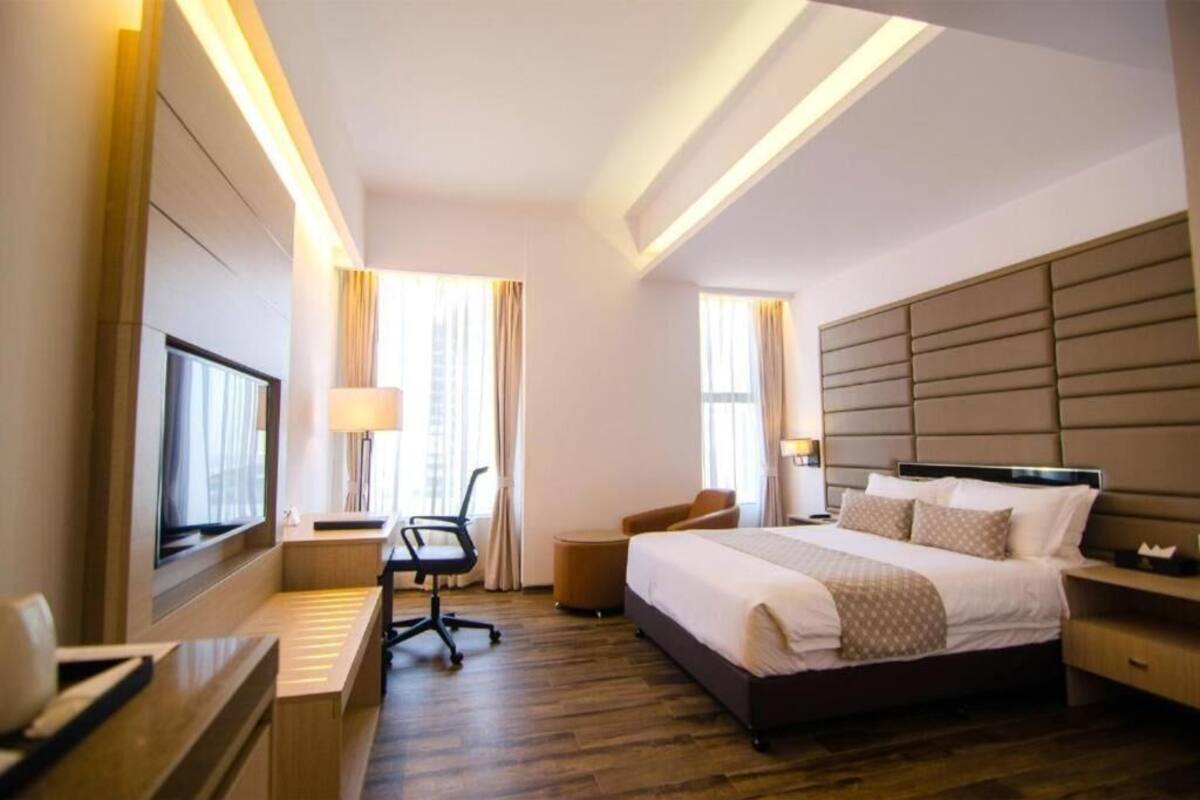 A hotel room with a large bed, a desk with a chair, a television, and a window with curtains.