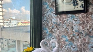 Una habitación con un ventanal grande, una obra de arte enmarcada y toallas dispuestas en forma de cisne sobre la cama.