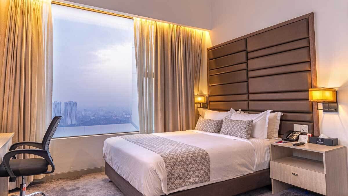 Habitación de hotel con una cama grande, un escritorio, una silla, una mesita de noche y vistas a la ciudad.