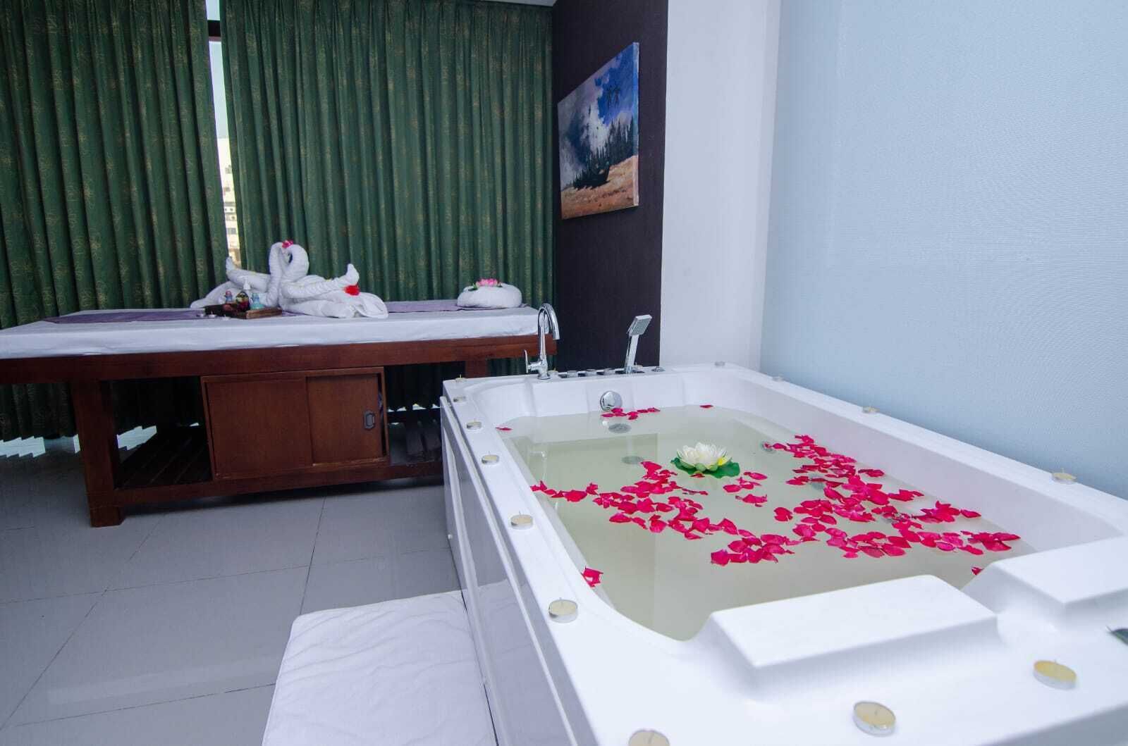 A bathroom with a bathtub filled with rose petals, a wooden vanity, and a painting on the wall.