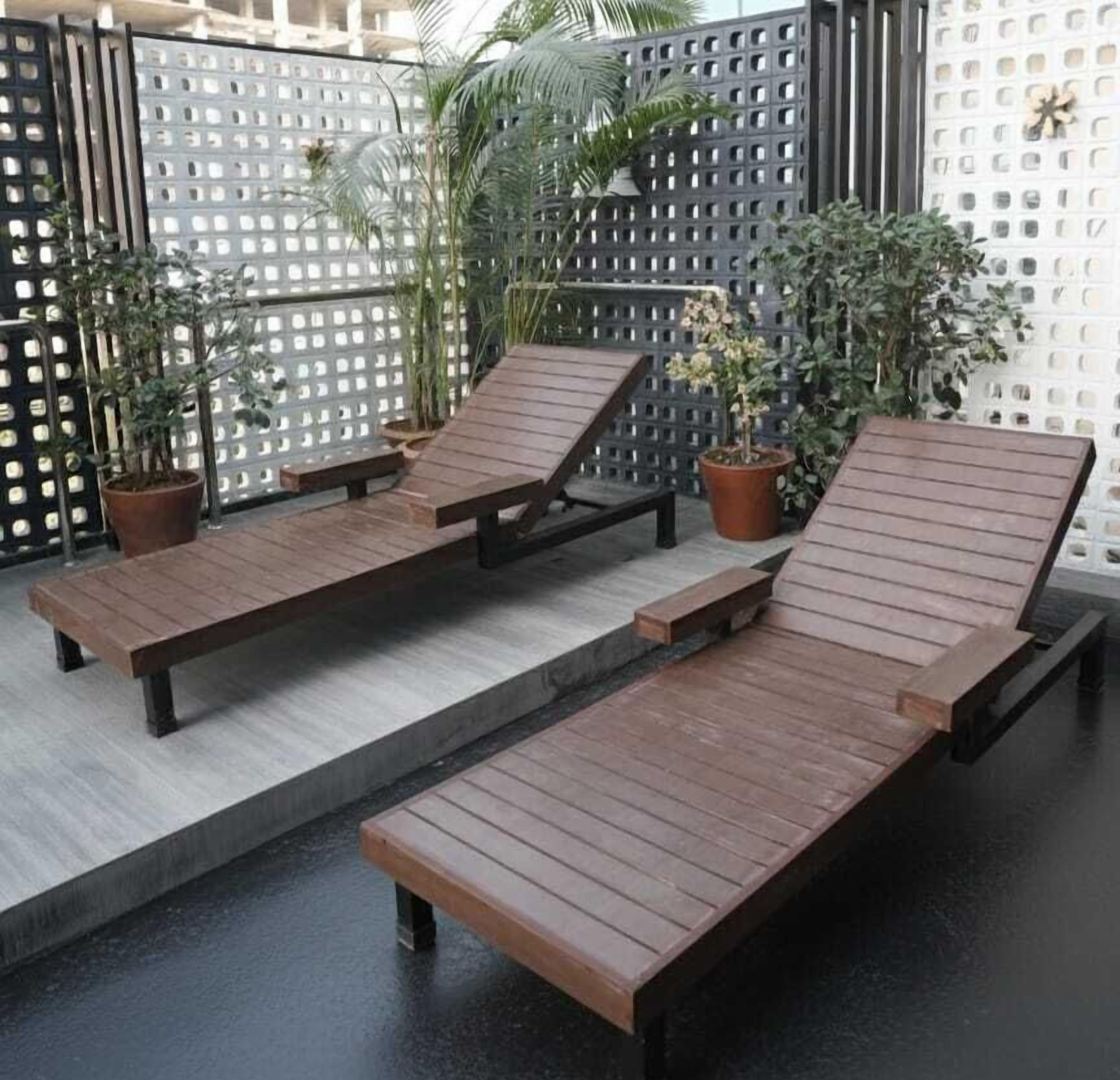 Uma área à beira da piscina com espreguiçadeiras de madeira e plantas em vasos.