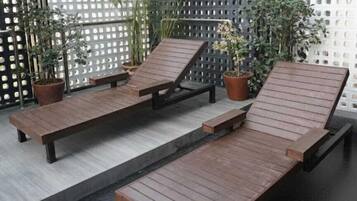Uma área à beira da piscina com espreguiçadeiras de madeira e plantas em vasos.
