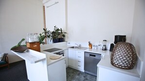 Una cucina funzionale con mobili bianchi, lavastoviglie, lavello e macchina da caffè. Sul piano di lavoro si trovano piante in vaso e una ciotola decorativa.