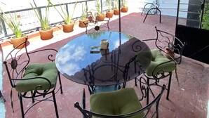 Un patio exterior con una mesa redonda y sillas, plantas en macetas y vistas de la ciudad.