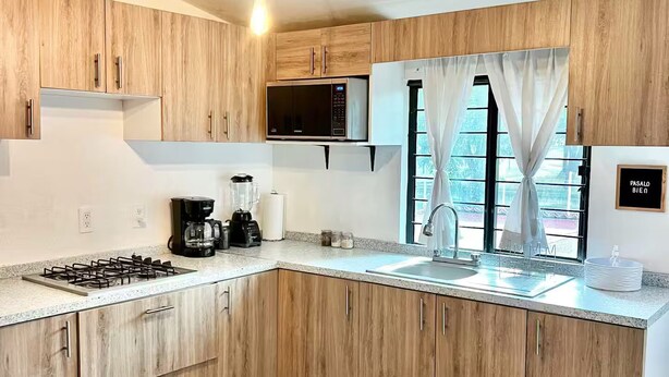 Una cocina moderna con armarios de madera, estufa a gas, microondas y un lavamanos. Hay una zona de comedor con una mesa y sillas.