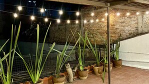 Un área con pavimento de ladrillo, plantas en macetas y luces colgantes.