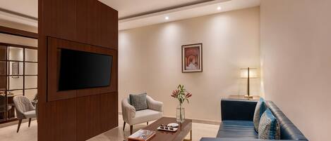 A modern living room with a flat-screen TV, a sofa, a coffee table, and a chair.