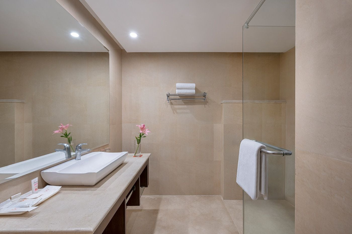 A modern bathroom with a large mirror, two sinks, a shower, and a towel rack.