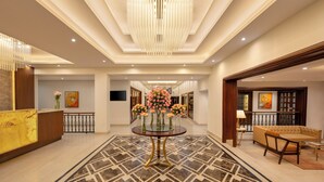 A spacious lobby with a central round table adorned with flowers, a chandelier, and a patterned floor.