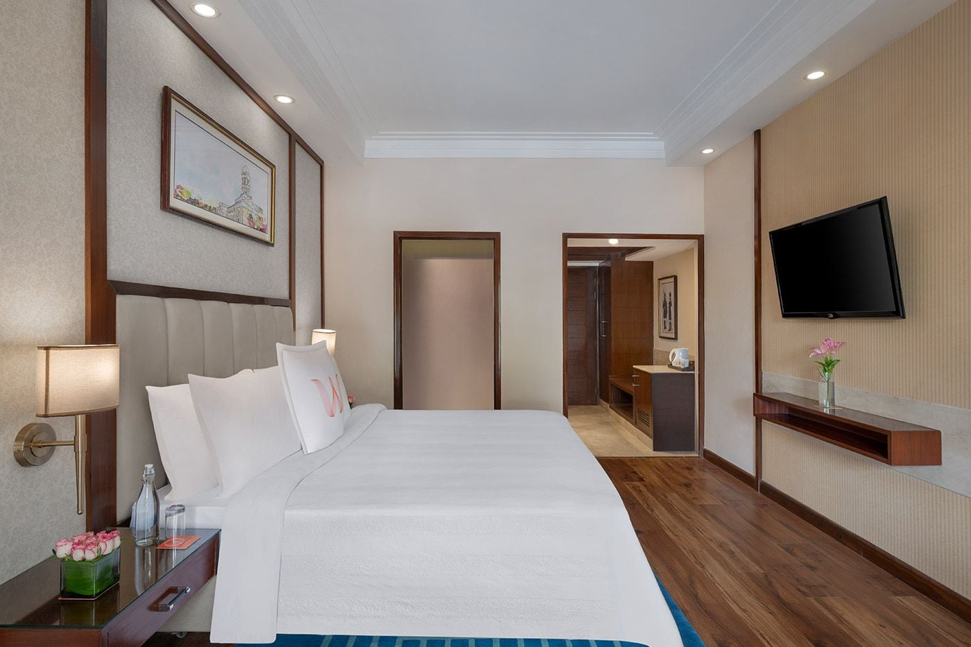 Habitación de hotel con una cama grande, un televisor montado en la pared y un baño visible a través de una puerta abierta.
