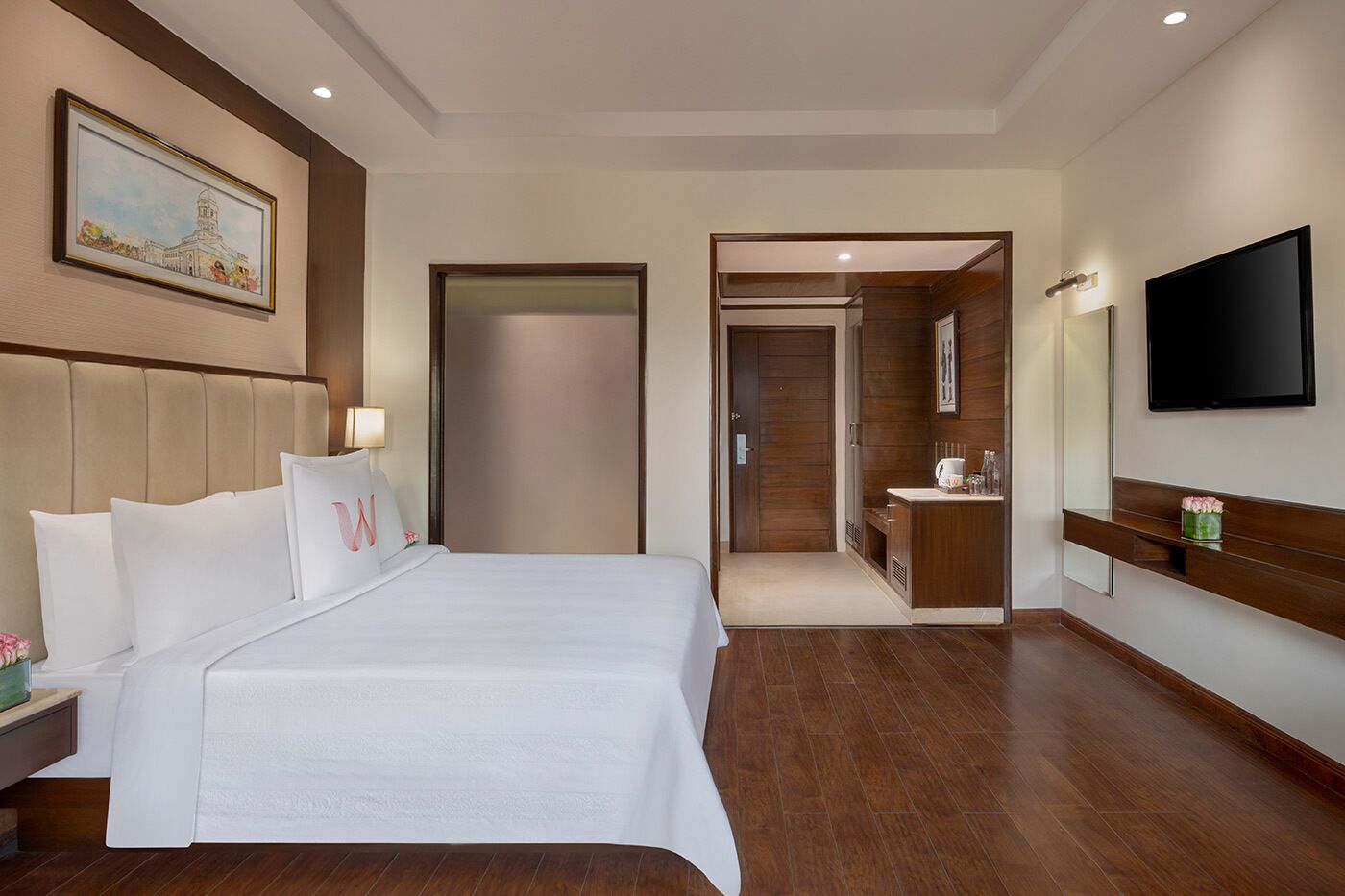 Habitación de hotel con una cama grande, un televisor, un baño con espejo y un cuadro en la pared.