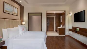 Habitación de hotel con una cama grande, un televisor, un baño con espejo y un cuadro en la pared.