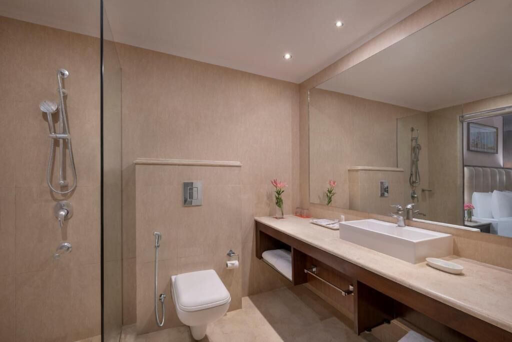 A modern bathroom with a glass shower enclosure, a white toilet, a large mirror, and a beige countertop.