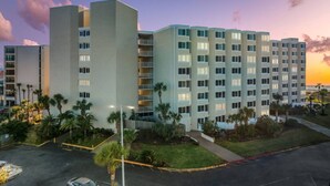 A multi-story hotel with a modern design, featuring a central courtyard with palm trees and a parking area. - Beach Front Ocean Front Condo Top of the Gulf 516 (Panama City Beach)