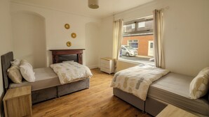 Ein Schlafzimmer mit zwei Betten, Holzboden, einem Fenster mit Vorhängen, einem Heizkörper und Blick auf ein Auto und ein Gebäude.