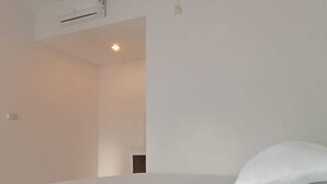 Ein schlicht eingerichtetes Hotelzimmer mit einem großen Bett, weißen Wänden und einer Decken-Klimaanlage.