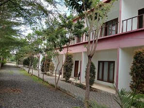 A row of two-story buildings with balconies, surrounded by trees and a gravel pathway. - Sisilia Lodge (Labuan Bajo)