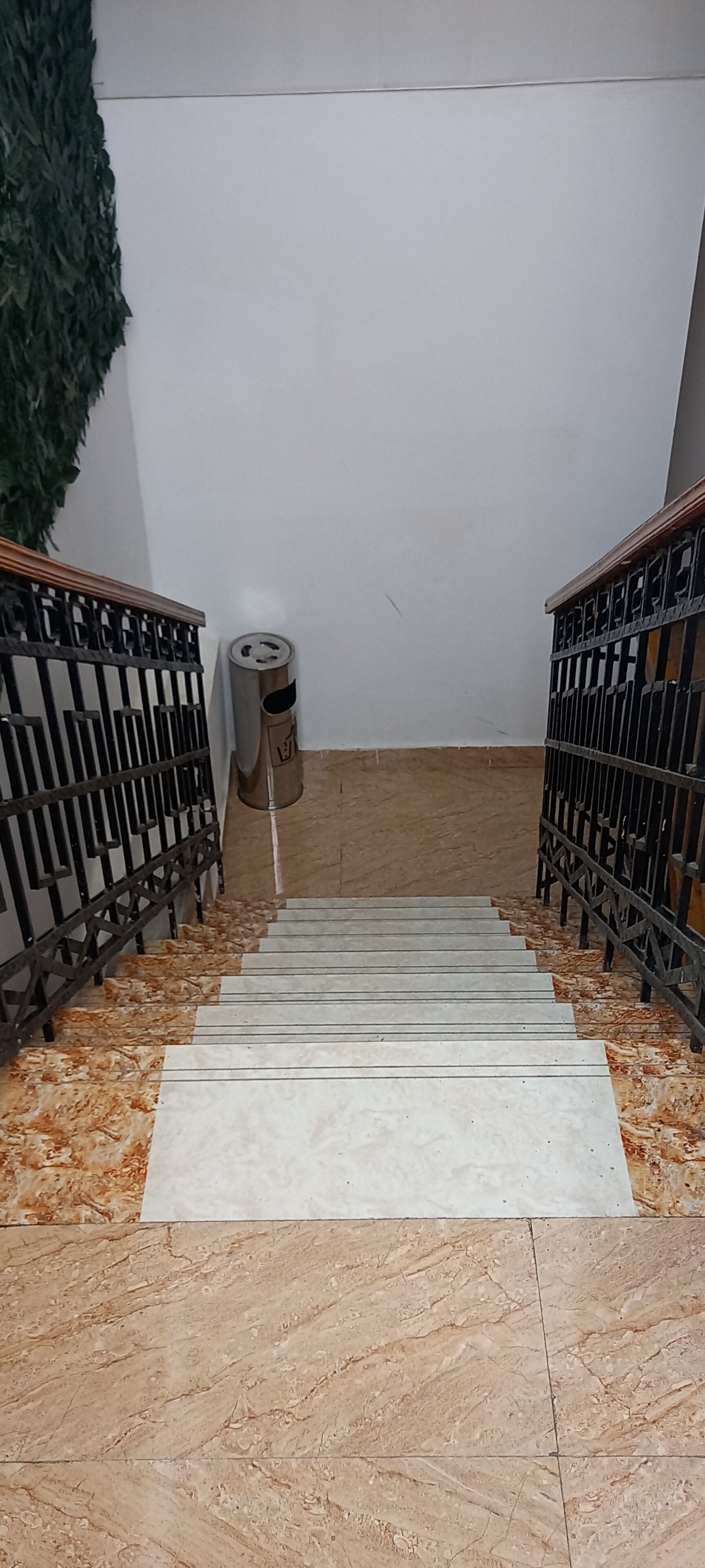 A staircase with metal railings, a trash can, and a wall with a green textured section.