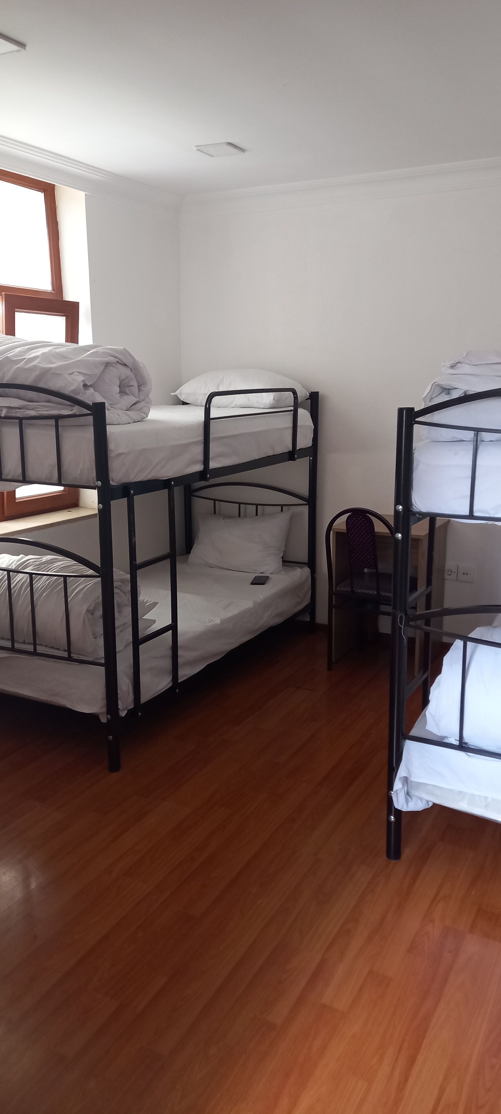 A room with bunk beds, wooden flooring, and a window.