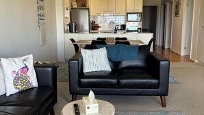 A modern living room with a black leather sofa, a round coffee table, and a kitchen in the background. - Bayview Encounter - Sea and island views in luxury incl breakfast and linen. (Encounter Bay)