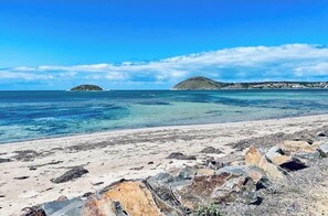 A beach with clear water, rocky foreground, and distant islands.