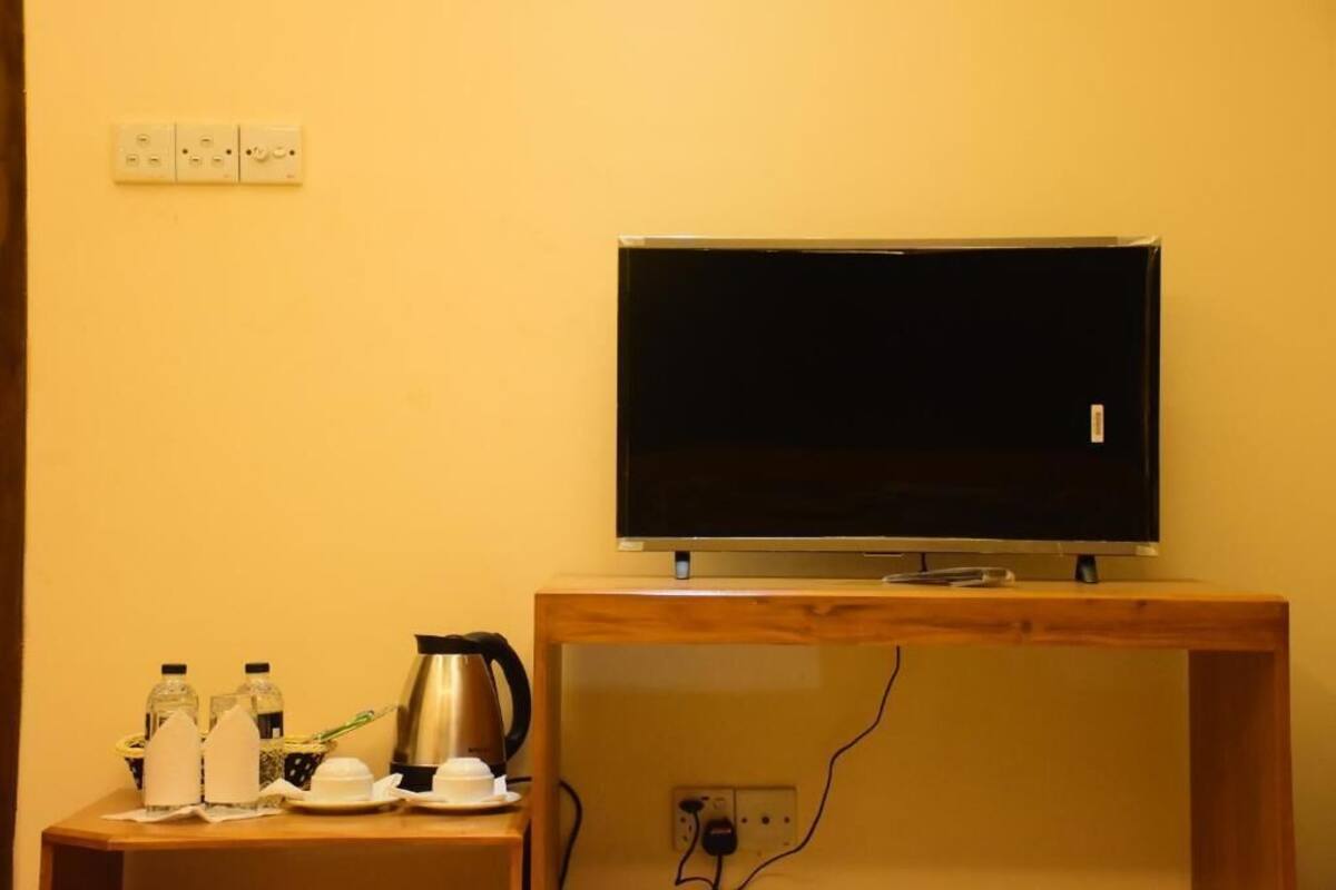 Un televisor sobre un soporte de madera, un enchufe y una mesita con una tetera, tazas y botellas.